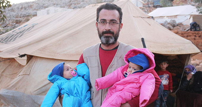 man holding two babies in syrian camp