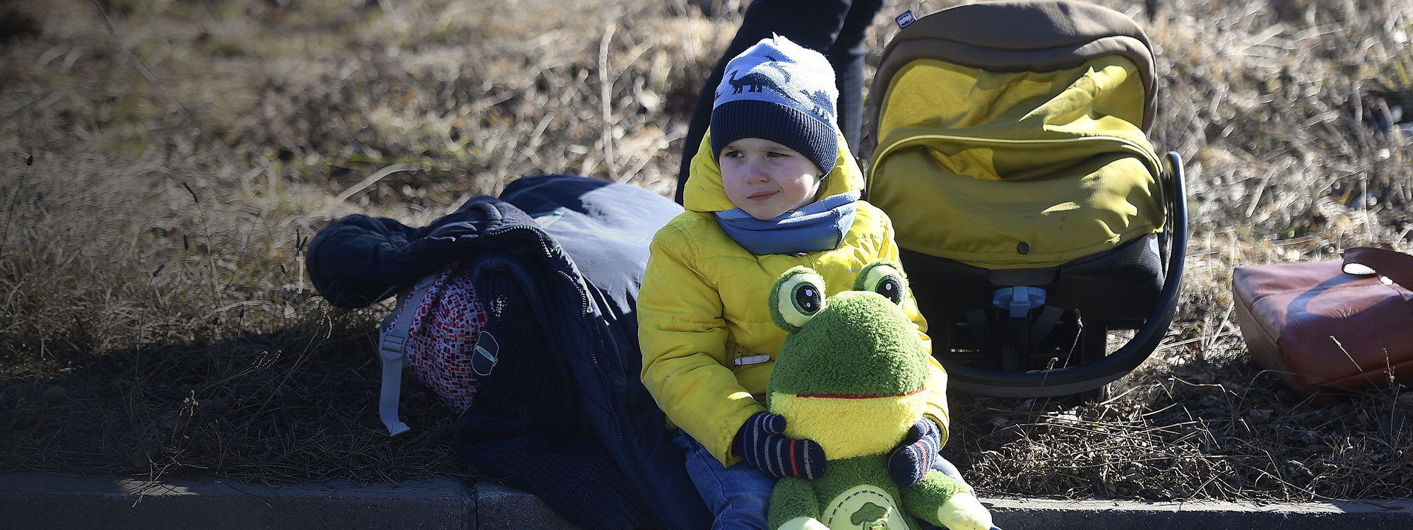 Ukrainian boy sits at the roadside in yellow jacket